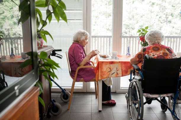 senior femenino desayunando cerca de la ventana, en la comunidad de retiro - atención residencial fotografías e imágenes de stock