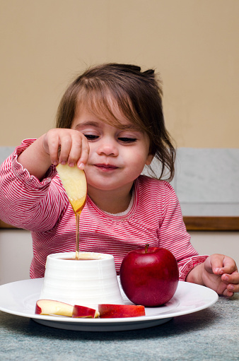 Little Jewish girl dips apple slices into honey during the most popular and well-known Jewish holiday Rosh HaShanah to express hope for a sweet new year.