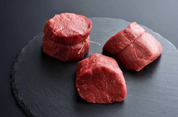 Three fresh raw Prime Black Angus Tenderloin beef steaks on stone background. Selected focus.