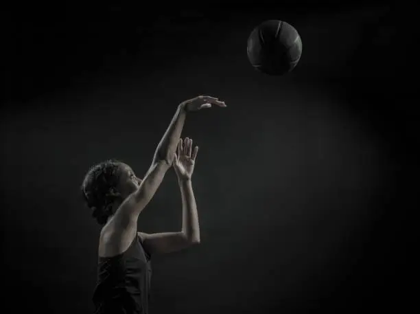 A desaturated image of an African Amercian women with a basketball on a black background.