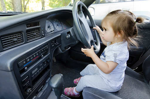 A little girl pretends to drive a car.