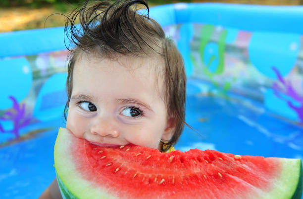 Weather Concept Photo - Heat Wave A baby girl eats cold watermelon in a baby pool on a very hot day. babyproof stock pictures, royalty-free photos & images