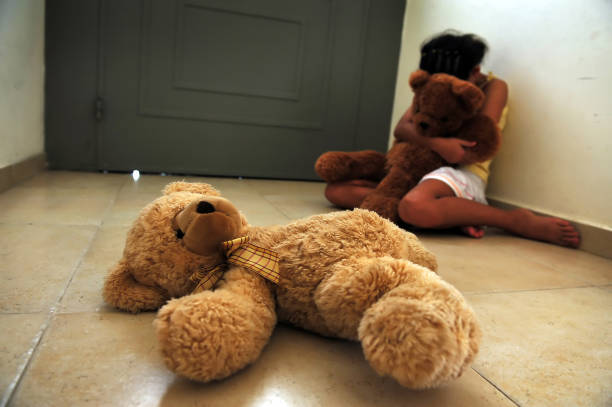 Young Girl Suffers from Domestic Violence A young girl who is a victim of domestic violence sits on the floor next to the front door and gets comfort from her teddy bears child abuse photos stock pictures, royalty-free photos & images