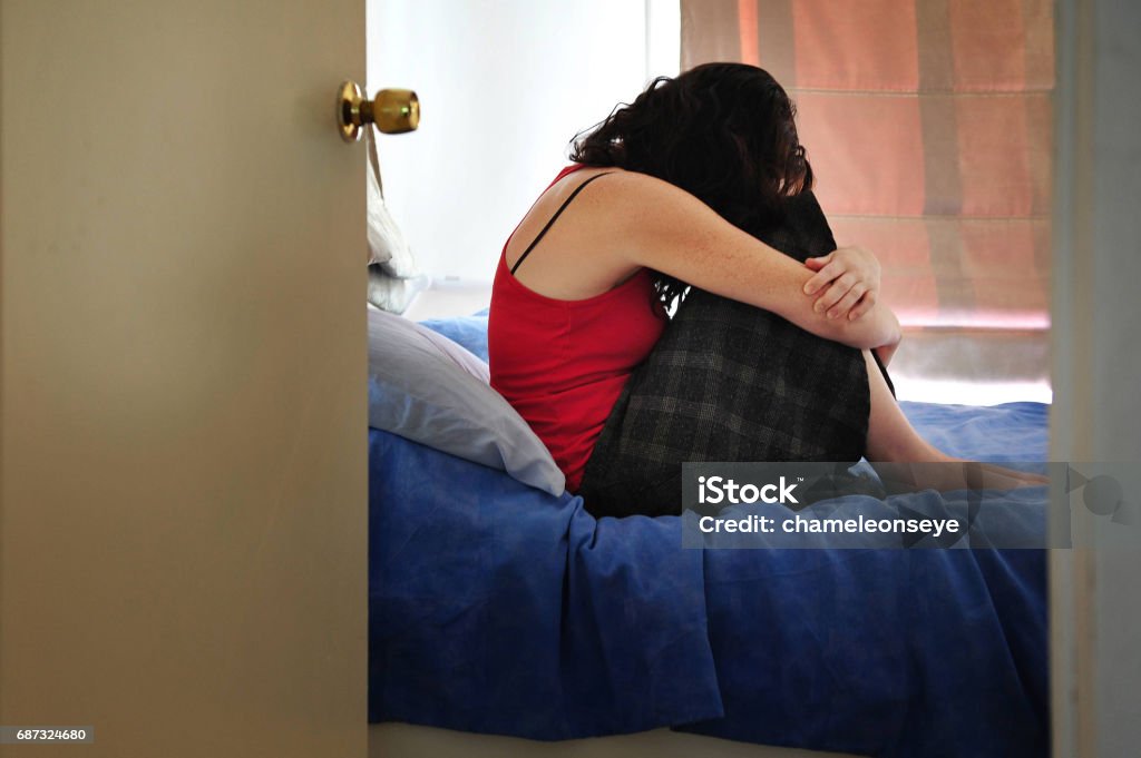 Depressed Woman Sits Cries on Bed Depressed young woman sitting on the bed at home suffering from a severe depression Domestic Violence Stock Photo