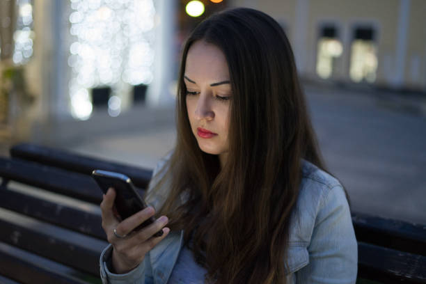 istock woman using smartphone sitting on the bench in night city 687359672