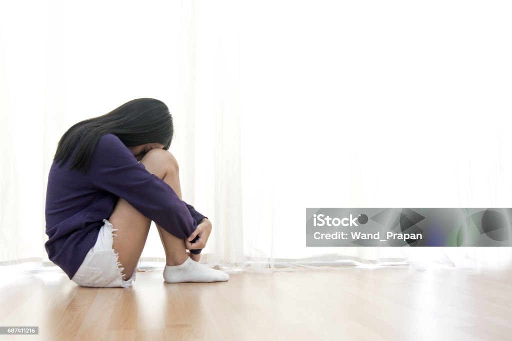 Sad young woman sit in her room and covering her face Sexual Harassment Stock Photo