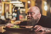 Obese male savoring grilled meat in pub