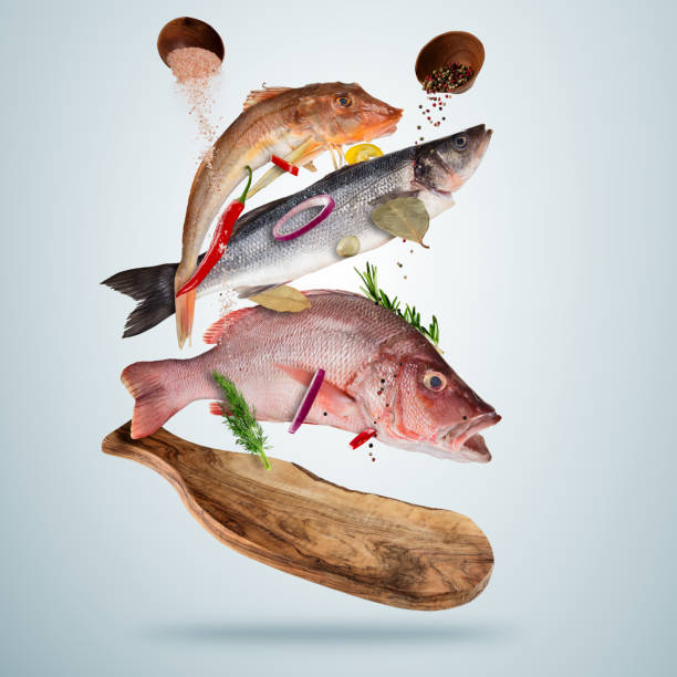 Fresh sea fish with falling spices, flying above wooden board, isolated on gray background. Food preparation, fresh meal ready for cooking. Extra high resolution