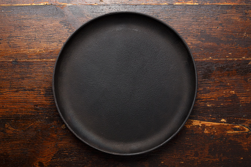 Empty round cast-iron pan for pizza on a brown wooden background, place for text