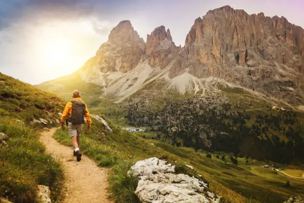 Senior man trail hiking on high mountain: by the Sella pass, with Saslong on background