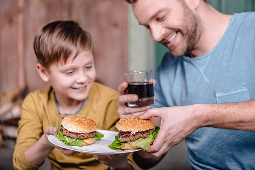 portrait of happy father and son holding plate with homemade burgers