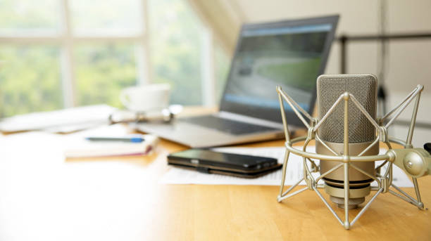 istock workspace for journalism with condenser microphone, laptop, cellphone and notepad on a desktop at the window, short panoramic banner for website headerwith blurred background, copy space 687441726
