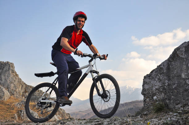istock Young man riding a bike on hill under a mountain 687449754