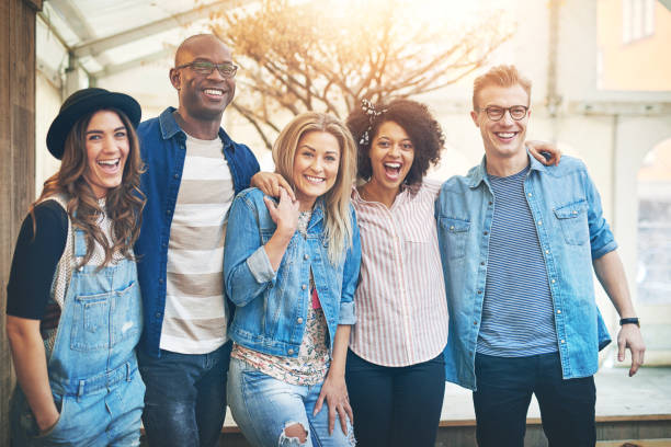 Five friends smiling to camera Group of beautiful young people in casual wear standing close together arms around, posing to camera laughing and smiling arm in arm stock pictures, royalty-free photos & images