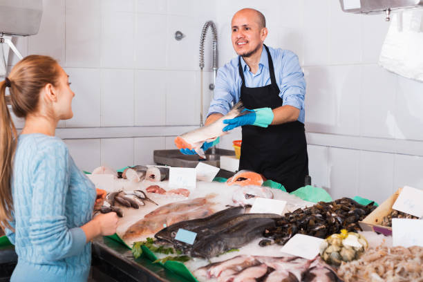 istock Smiling seller helping female customer to choose fish 687471646