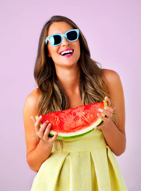 Studio shot of a beautiful woman holding a watermelon against a pink background