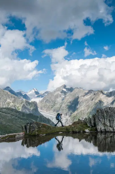 Female Hiker walking across a lake wall with the European Alps and her reflection in the water