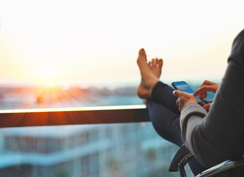 Woman using phone and relaxing at end of the day with feet up