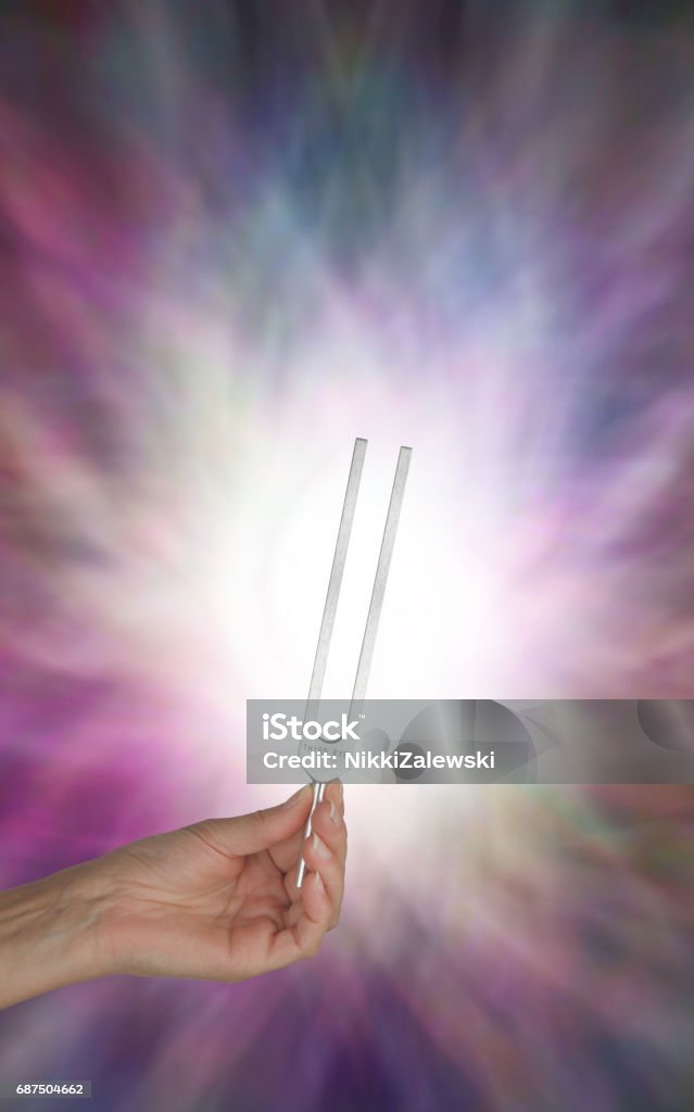 Holding Tuning Fork in Resonating Energy Field Female hand holding Tuning Fork upright with light behind and Resonating Energy Field Tuning Fork Stock Photo