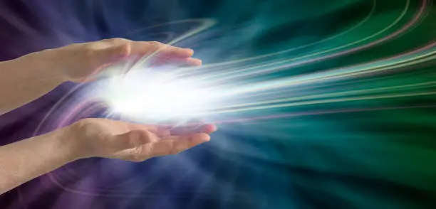 Parallel female hands with a swirling light burst between on a dark blue, purple and green energy field background