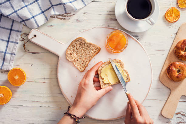 frau hand streut butter auf geschnittenem brot - butter stock-fotos und bilder