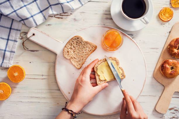 mão da mulher que espalha a manteiga no pão cortado - butter bread breakfast table - fotografias e filmes do acervo
