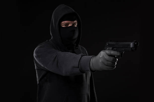 istock The robber in a mask with a gun pointed to the side on a black background 687524252