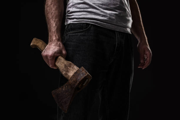 A man holds an ax in his hands against on black background. Criminal