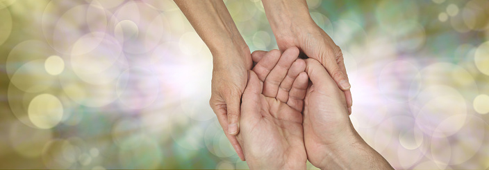 Wide banner with a woman's hands holding a man's cupped hands in a needy gesture on a bokeh and light burst background and plenty of copy space either side