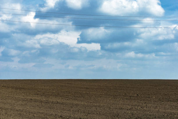 istock Plowed field, fertile, black soil ready for sowing. Blue spring sky two pillars of high voltage. 687540734