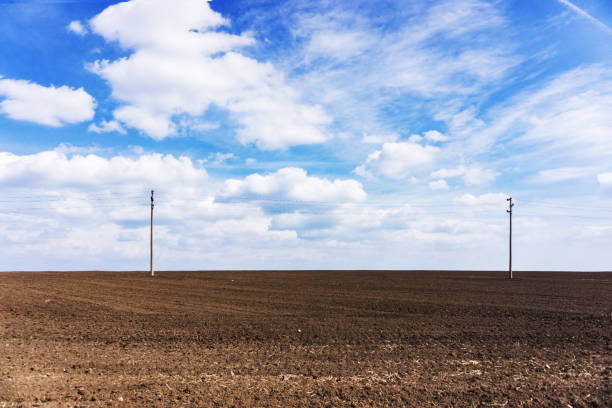 istock Plowed field, fertile, black soil ready for sowing. Blue spring sky two pillars of high voltage. 687540872