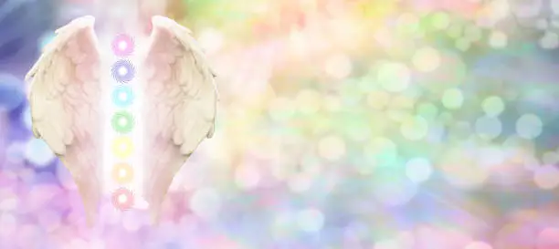 Angel wings and seven chakras on pastel rainbow colored bokeh  background with copy space on right hand side