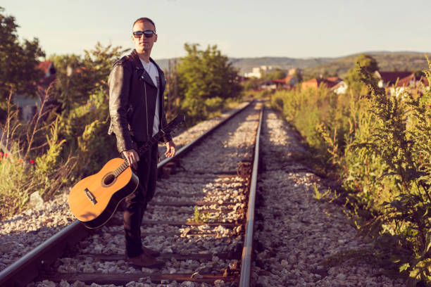 Musician with leather jacket and a guitar on the railway