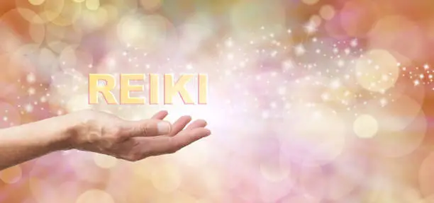 Female with outstretched hand palm facing up and the word 'REIKI' hovering above  on an ethereal golden bokeh and sparkles background and white light