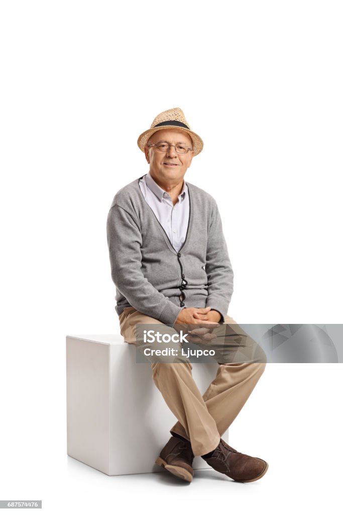 Senior sitting on a cube Senior sitting on a cube and looking at the camera isolated on white background Sitting Stock Photo