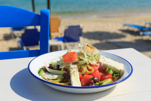 Ensalada griega por el mar, la tradicional ensalada griega de fondo de la tabla de madera blanca, silla Defocused y playa en el fondo - foto de stock
