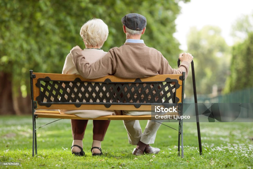 Pareja de ancianos sentada en un banco de madera en el parque - Foto de stock de Tercera edad libre de derechos
