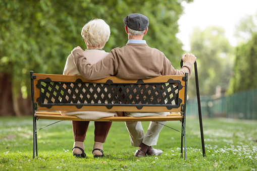 Outdoor portrait of happy senior couple sitting on steps outside house, smiling at camera.