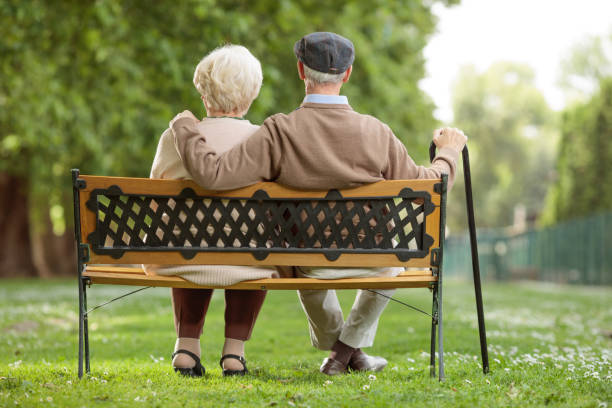 Senior couple sitting on a wooden bench in the park Rear view shot of a senior couple sitting on a wooden bench in the park bench stock pictures, royalty-free photos & images