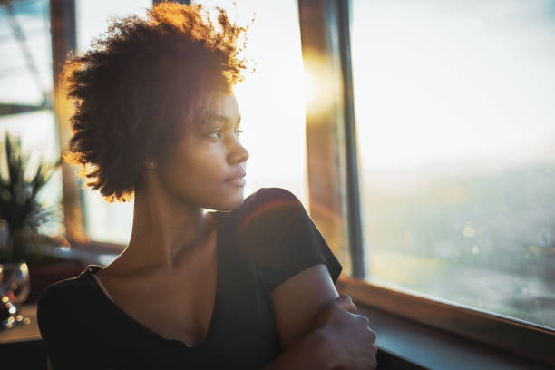 Black teenage female in cruise ship Curly charming young afro american tourist female in black dress is sitting in luxury restaurant of cruise ship near window and thoughtfully looking out the big window on ocean and warm sunset horizon cruise ship people stock pictures, royalty-free photos & images