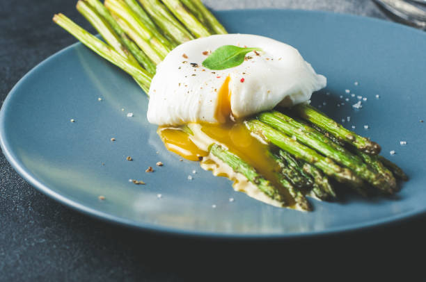 istock Green asparagus and boiled poached egg on a blue plate over a dark concrete background 687602376