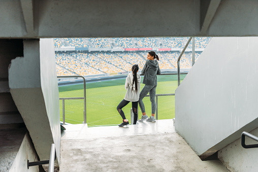 full length of two young sportswomen standing at handrail on stadium