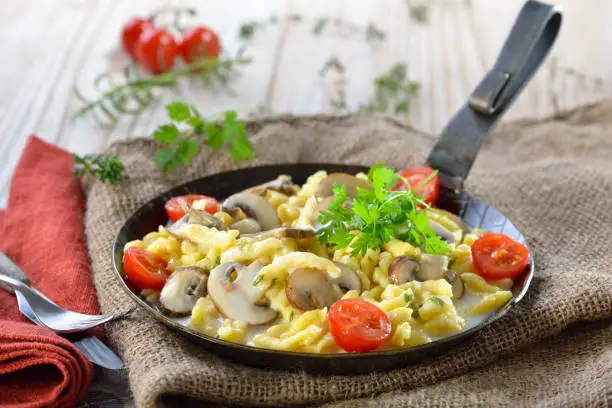 Vegetarian Swabian spaetzle with thickened cream sauce and fresh mushrooms served in an iron frying pan on a rustic table with an old jute sack