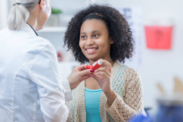 African American teenage girl learns to use inhaler African American teenage girl with asthma learns to use inhaler. A senior female doctor is instructing her on the proper use of the inhaler. pretty girl using asthma inhaler stock pictures, royalty-free photos & images