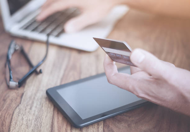 istock man sitting at rustic wood desk holding a credit card while typing on a laptop computer 687678088
