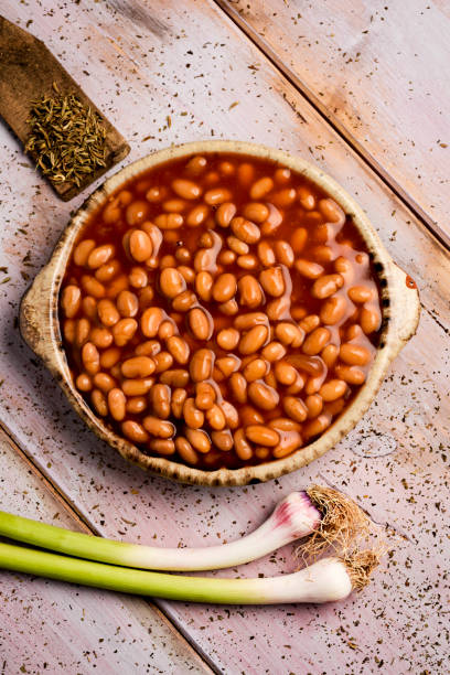 baked beans high-angle shot of an earthenware bowl full of baked beans and some green garlics on a rustic wooden table baked beans stock pictures, royalty-free photos & images