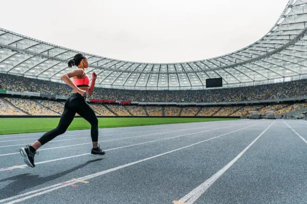 Athletic young woman in sportswear sprinting on running track stadium