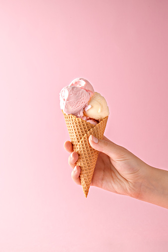 Mano de mujer sosteniendo un cono de helado sobre un fondo rosa. photo