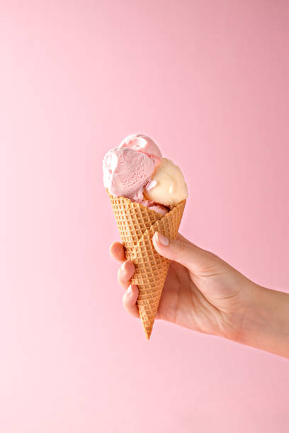 mano de mujer sosteniendo un cono de helado sobre un fondo rosa. - ice cream cone fotografías e imágenes de stock