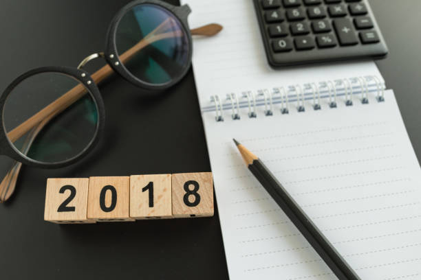 istock financial target concept as selective focus on number 2018 wooden block with glasses, calculator, pencil, notebook. 687686054
